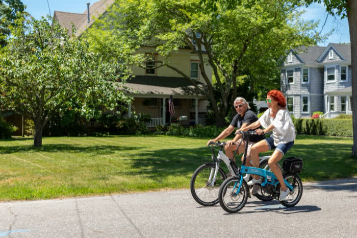 Two people riding bikes along a tree-lined street